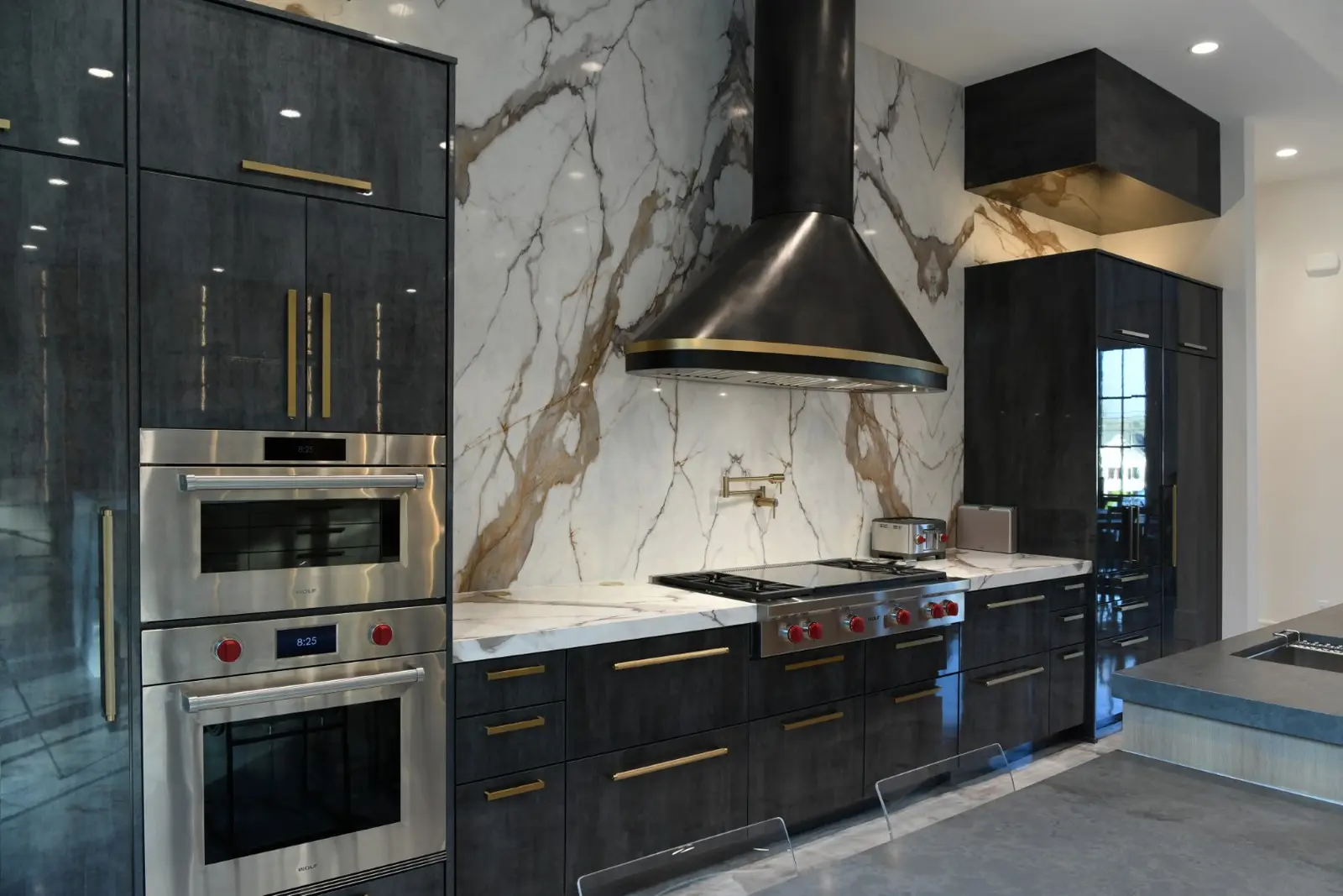 Sever Residence kitchen with dark cabinetry, brass pulls, and a marble slab backsplash